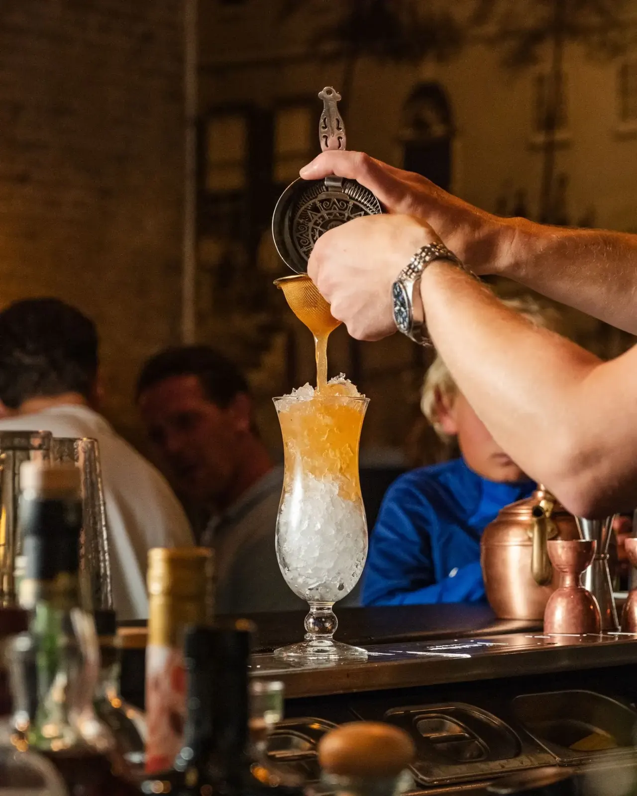 Een oranje cocktail wordt ingeschonken in een hoog glas met ijs