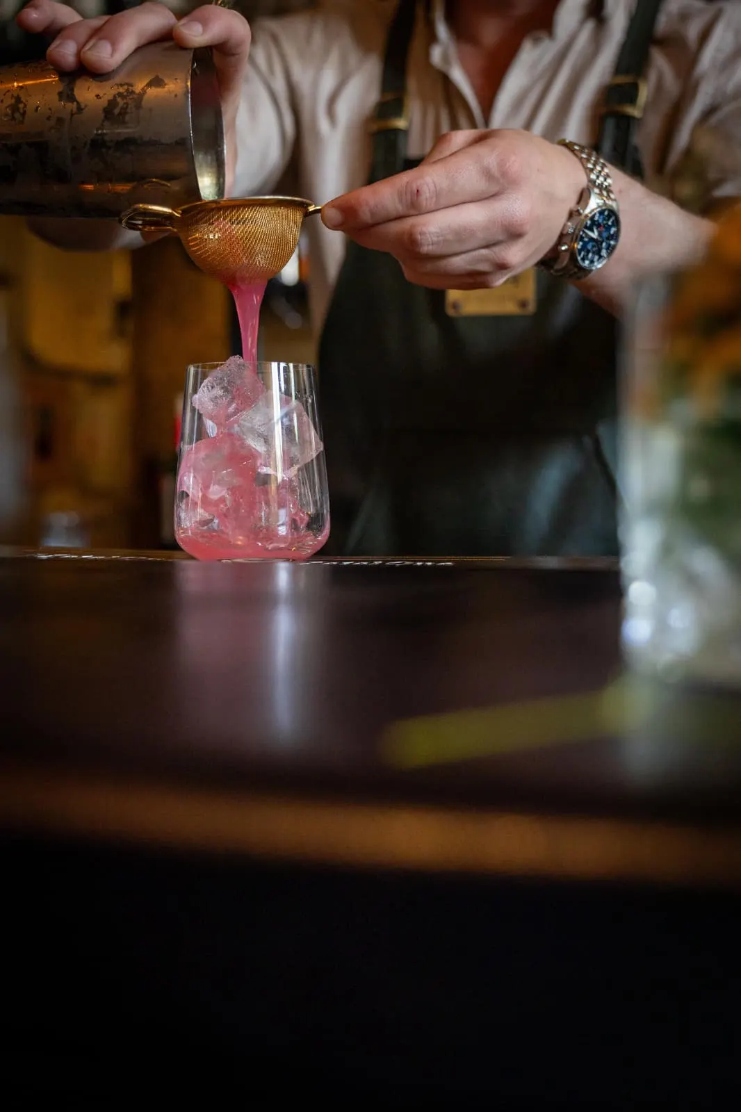 Jasper schenkt een roze cocktail door een zeef in een glas met ijs