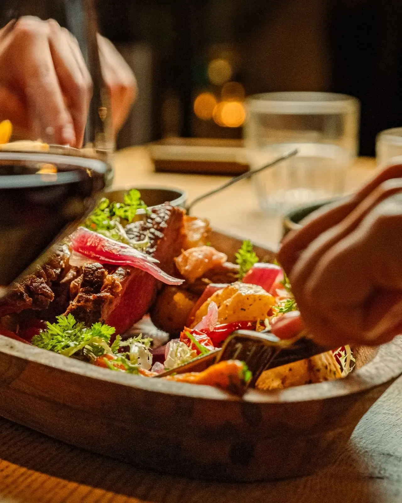 Gasten delen een gerecht op een houten schaal aan tafel